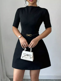 Person wearing a black dress holding a white handbag against a neutral background