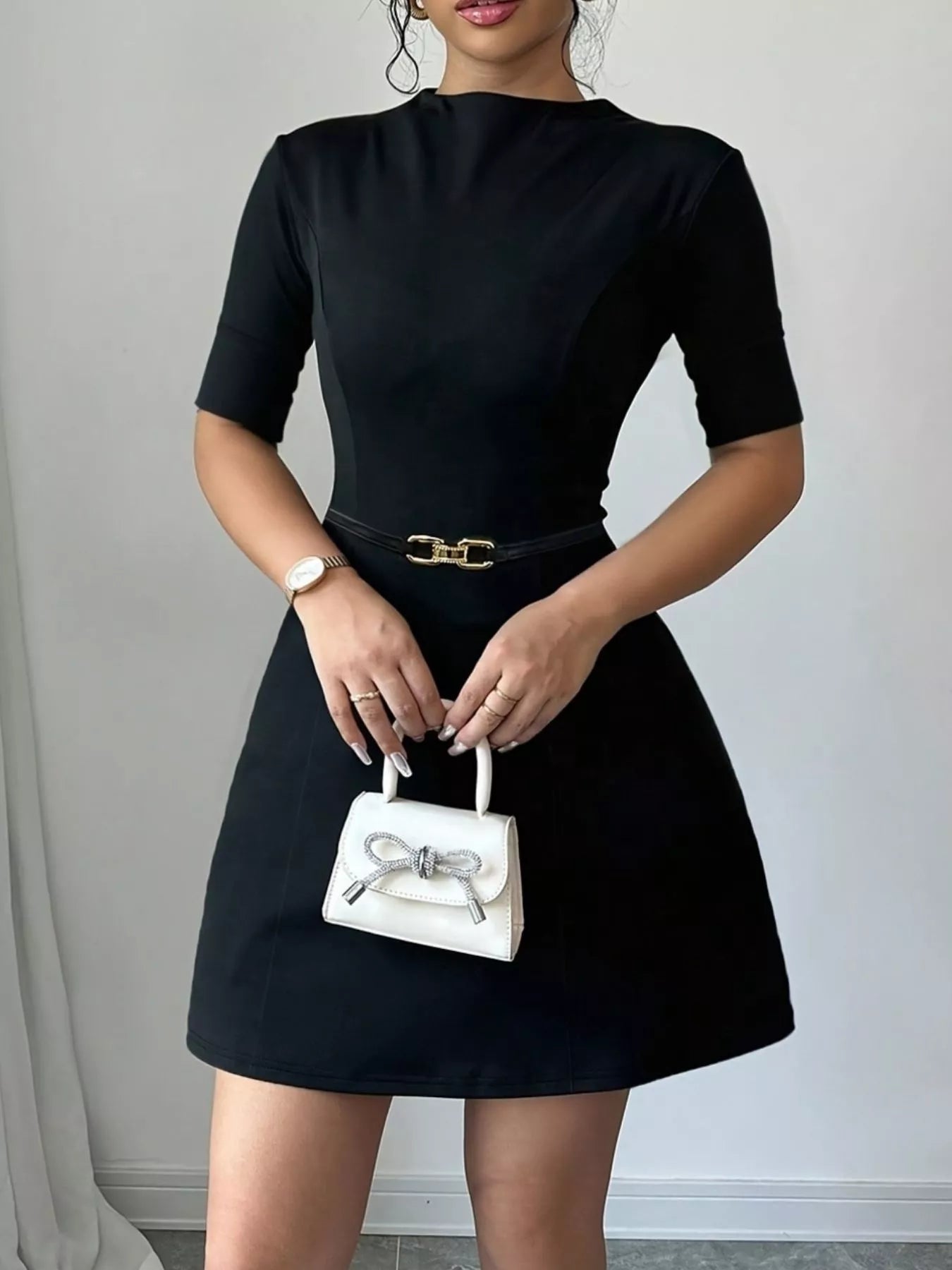 Person wearing a black dress holding a white handbag against a neutral background