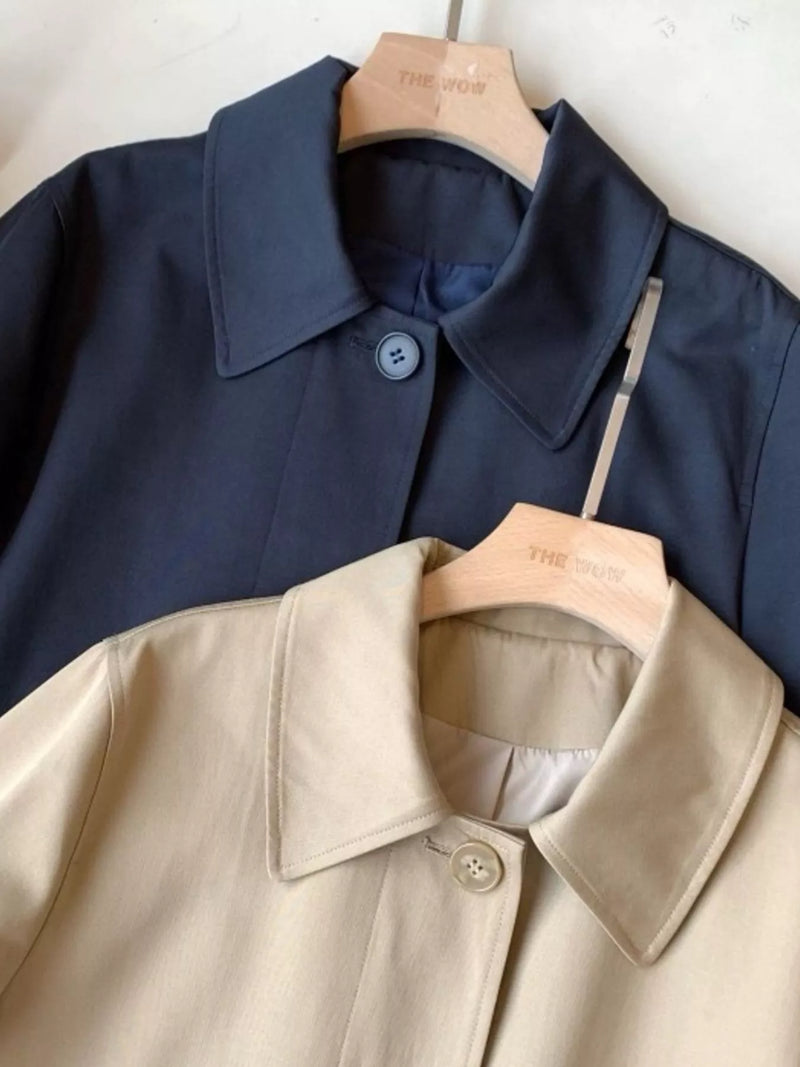 Two collared button-front jackets hanging on wooden hangers against a light wall. The upper jacket is dark navy blue and the lower jacket is light beige.