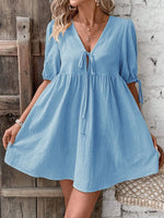Woman wearing a blue dress standing against a wooden and brick wall.