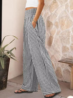 Person wearing black and white checkered pants standing against a stone wall.