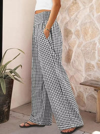 Person wearing black and white checkered pants standing against a stone wall.