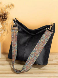 Black handbag with a patterned strap on a wooden surface