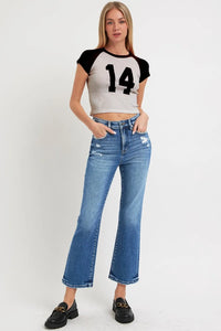 Woman wearing a crop top with the number 14 and high-waisted jeans on a white background