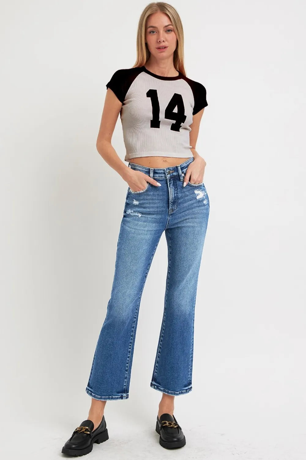 Woman wearing a crop top with the number 14 and high-waisted jeans on a white background