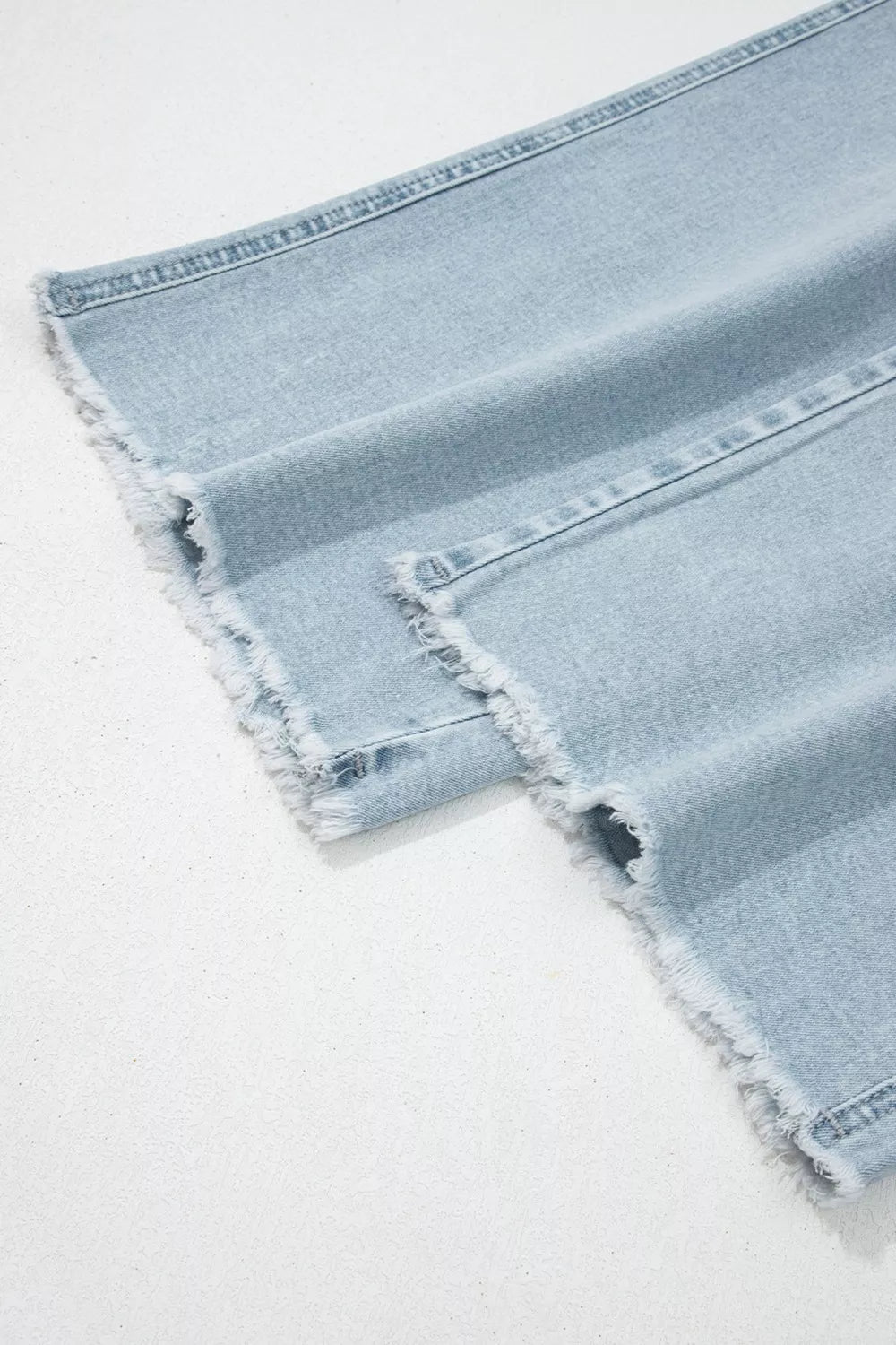 Light blue denim fabric with frayed edges on a white background