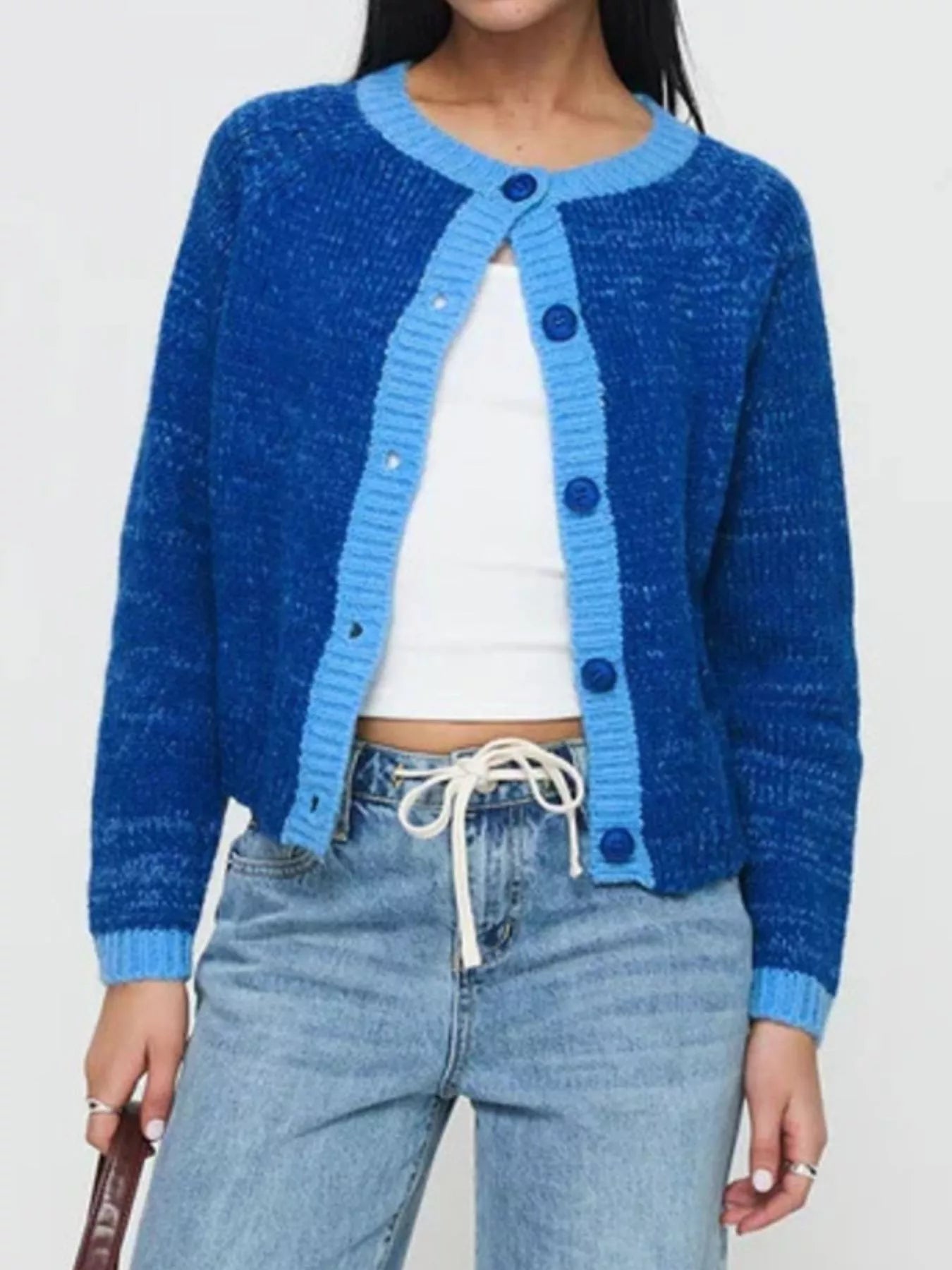 Person wearing a blue cardigan over a white top and jeans on a plain background