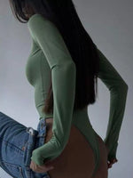 Person wearing a green bodysuit and blue jeans against a plain background