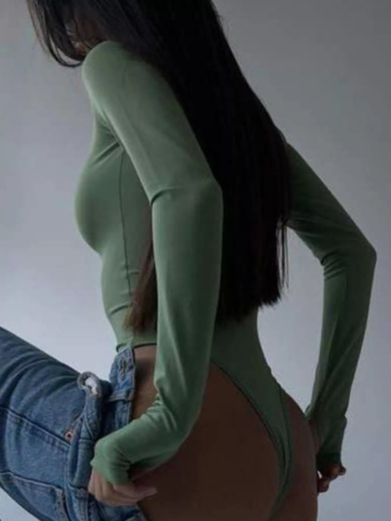 Person wearing a green bodysuit and blue jeans against a plain background