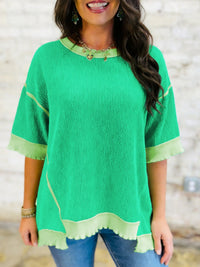 Woman wearing a green top with yellow trim against a neutral background
