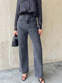 Person wearing black satin shirt and gray high-waisted jeans against a concrete wall.