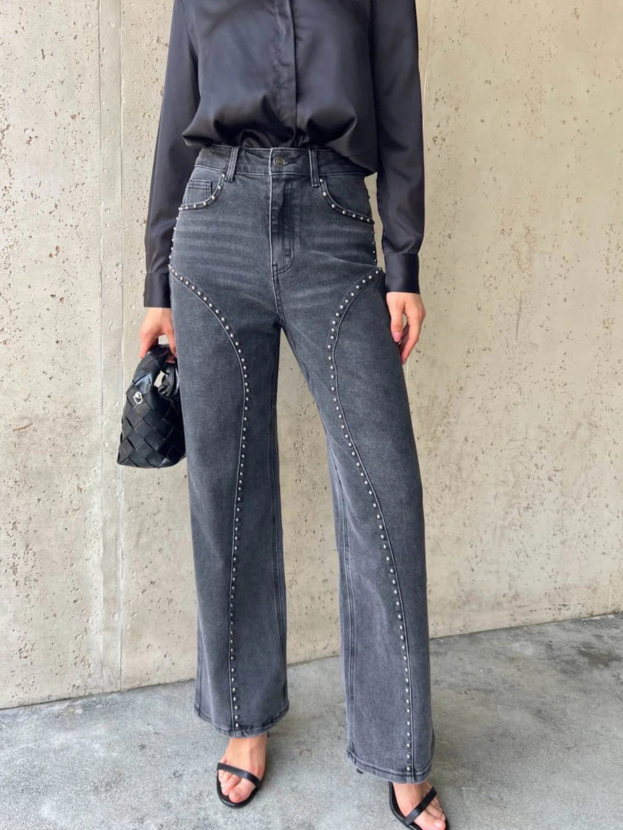 Person wearing black satin shirt and gray high-waisted jeans against a concrete wall.