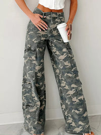 Person wearing camouflage cargo pants holding a white cup against a plain background