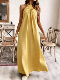 Person wearing a yellow dress in a room with wooden chairs and a mirror.