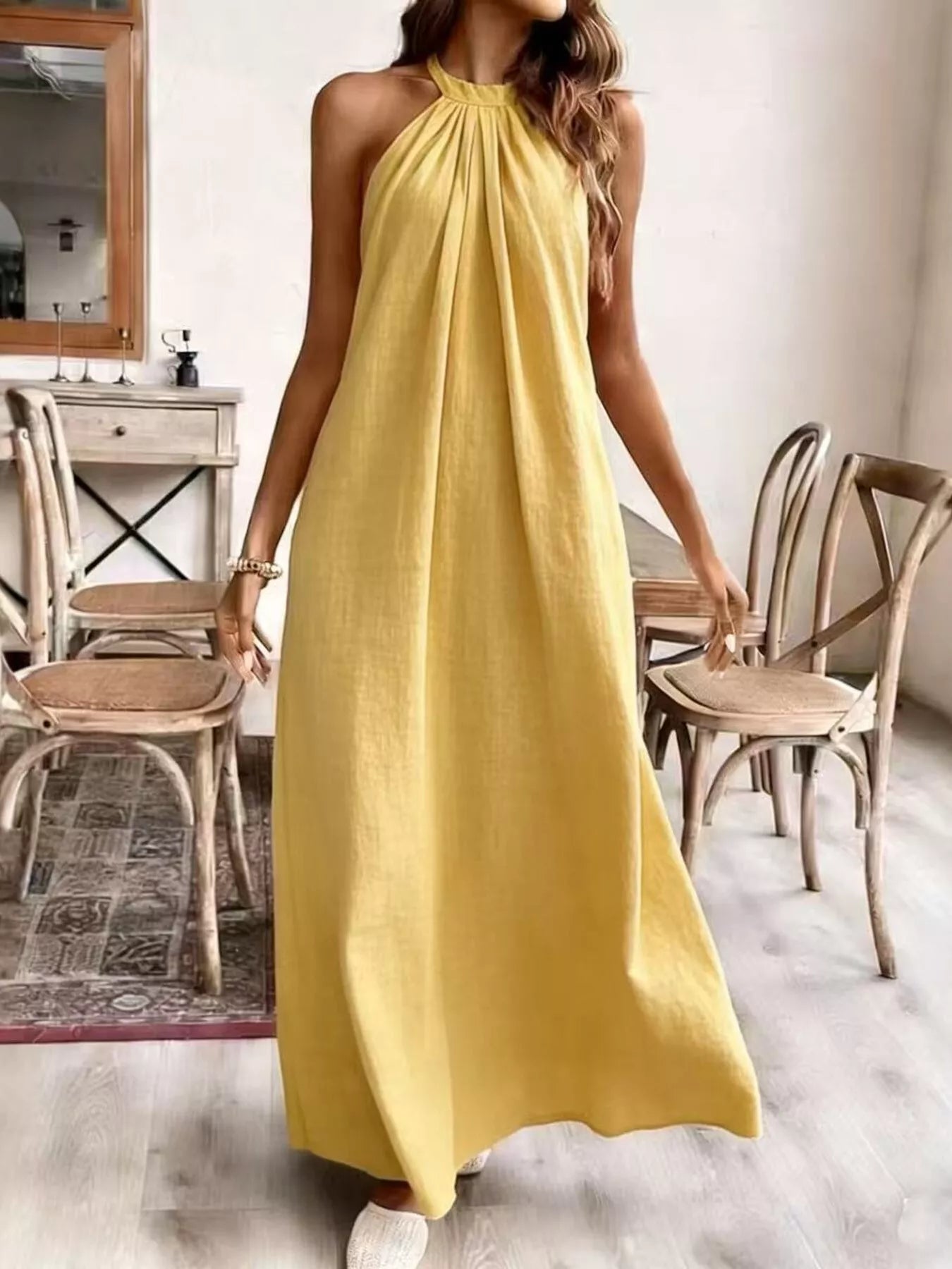 Person wearing a yellow dress in a room with wooden chairs and a mirror.
