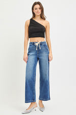 Woman wearing a black one-shoulder top and blue jeans on a white background