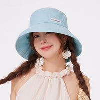 Woman wearing a light blue bucket hat with a visible brand logo on a white background