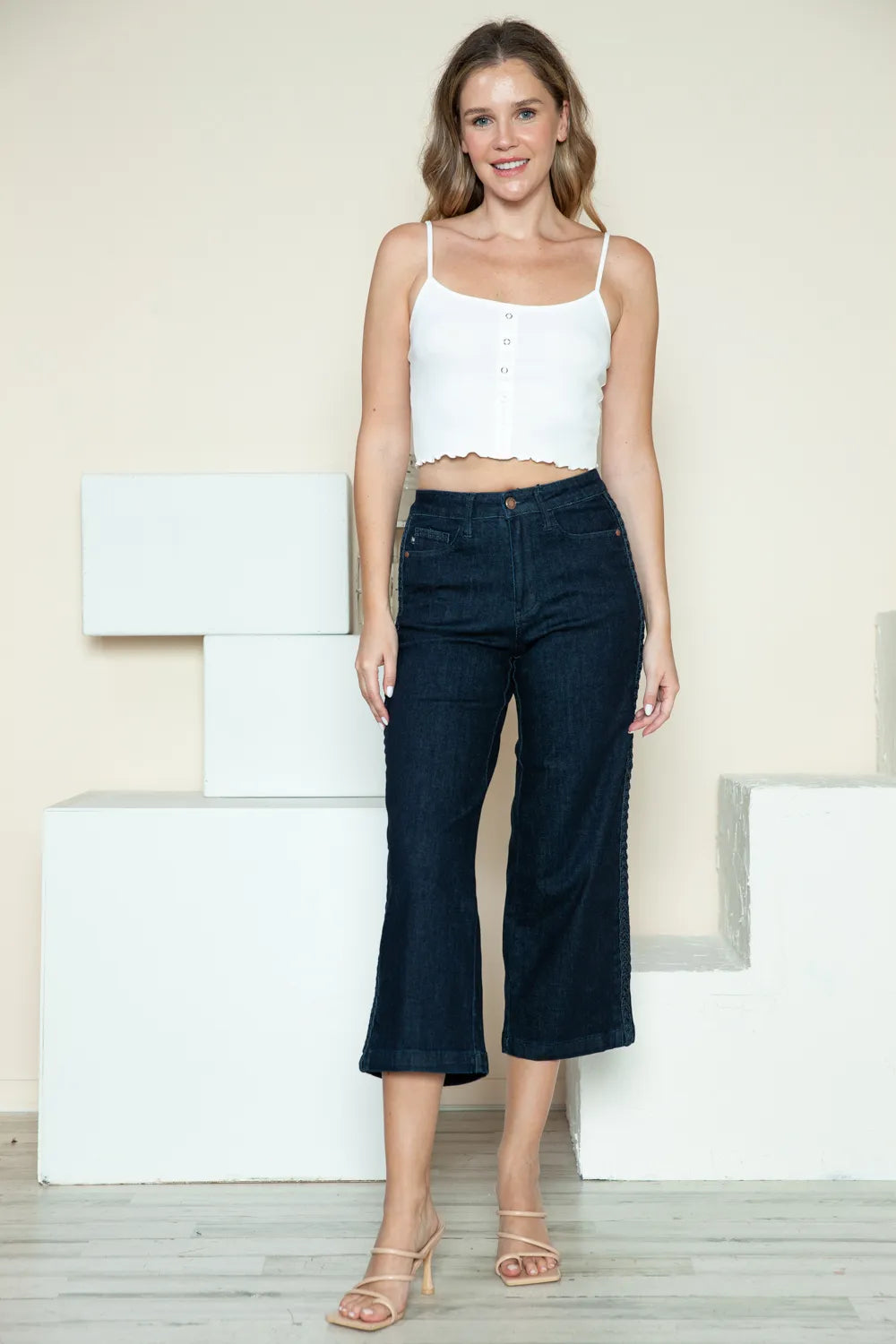 Woman wearing a white top and dark blue jeans standing on white steps.