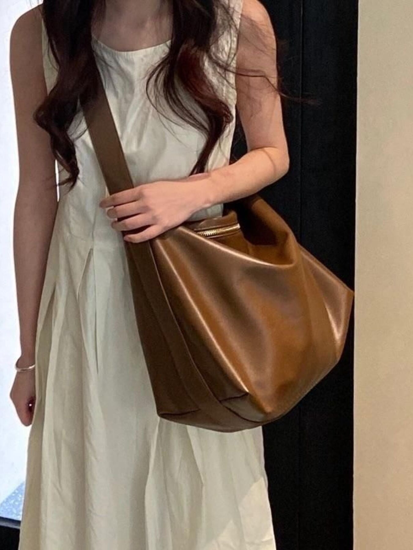 Woman holding a brown leather handbag against a neutral background