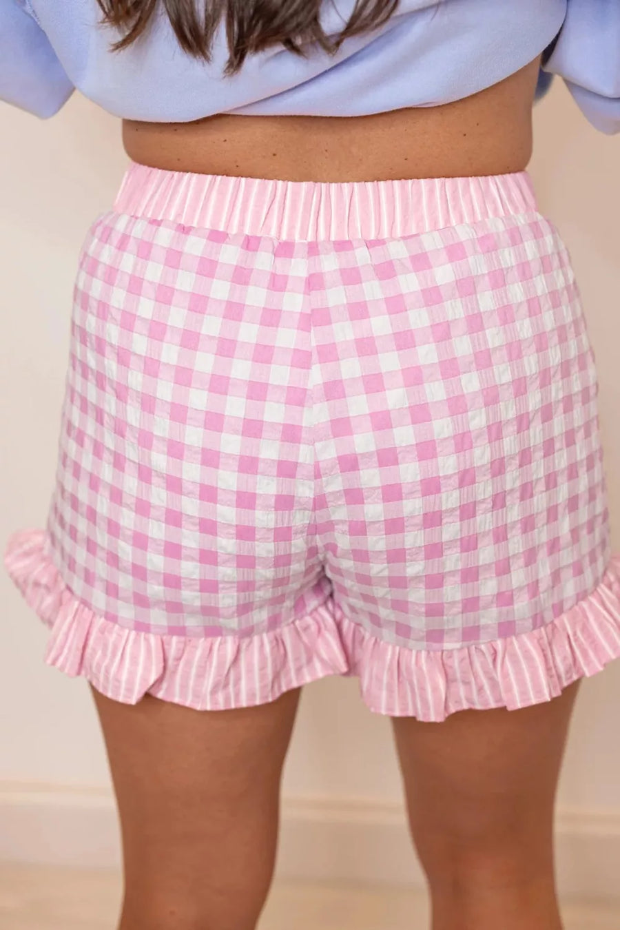 Pink gingham shorts with ruffle details worn by a person.