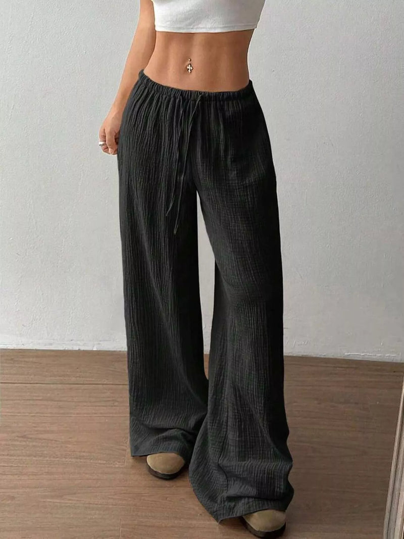 Person wearing dark wide-leg pants with a plain background