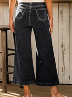 Person wearing black wide-leg jeans standing in a rustic setting.
