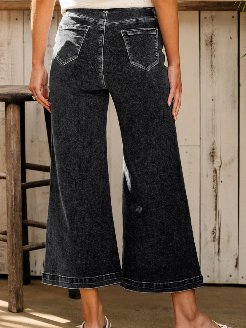 Person wearing black wide-leg jeans standing in a rustic setting.