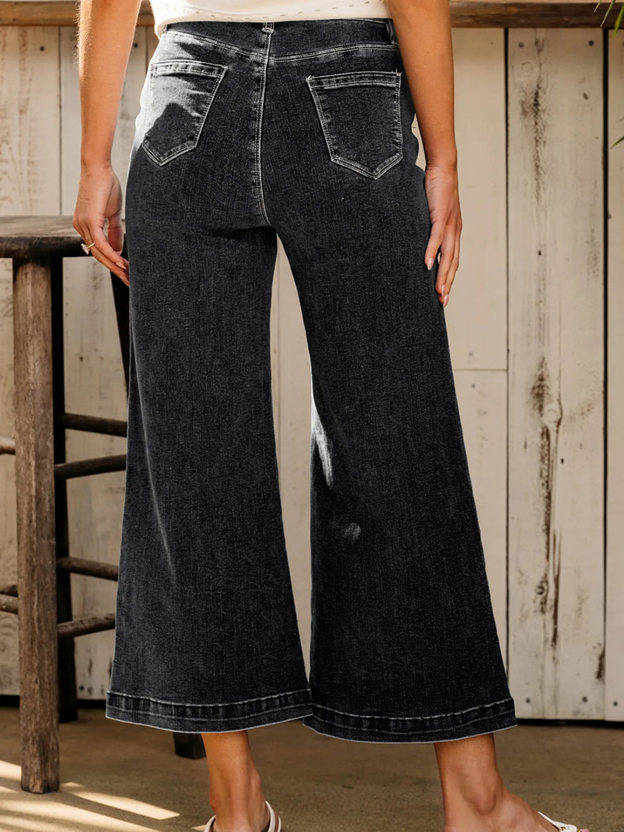 Person wearing black wide-leg jeans standing in a rustic setting.