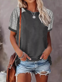 Woman wearing a gray and green short-sleeve shirt with denim shorts against a neutral background