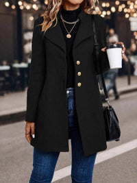 Person wearing a black coat with gold buttons, holding a coffee cup on a street.