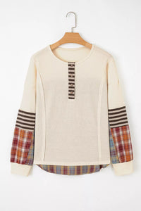 Beige sweater with plaid sleeves on a wooden hanger against a white background