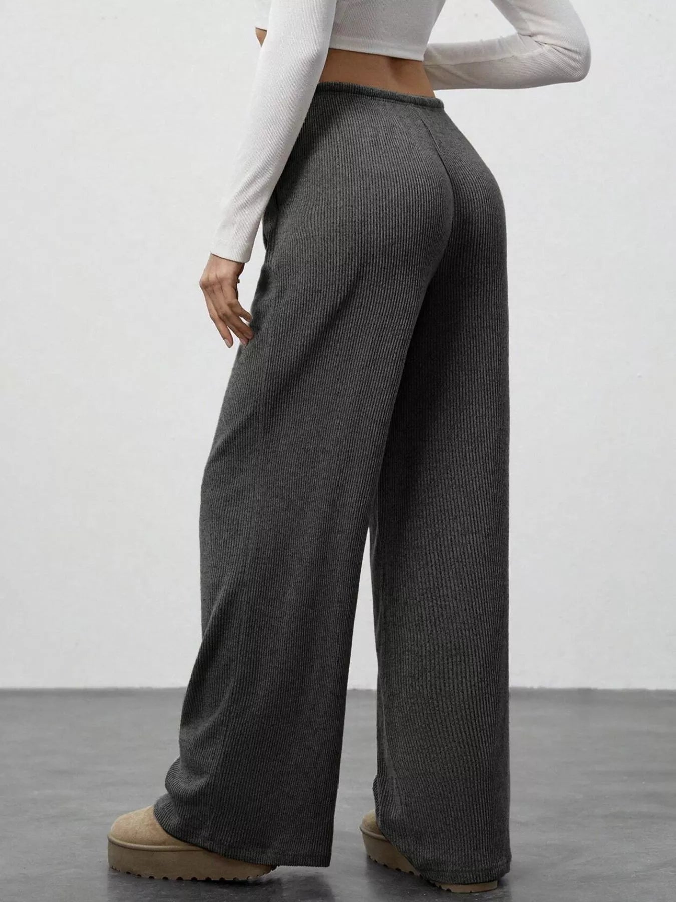 Person wearing dark ribbed wide-leg pants and a white long-sleeve top on a plain background