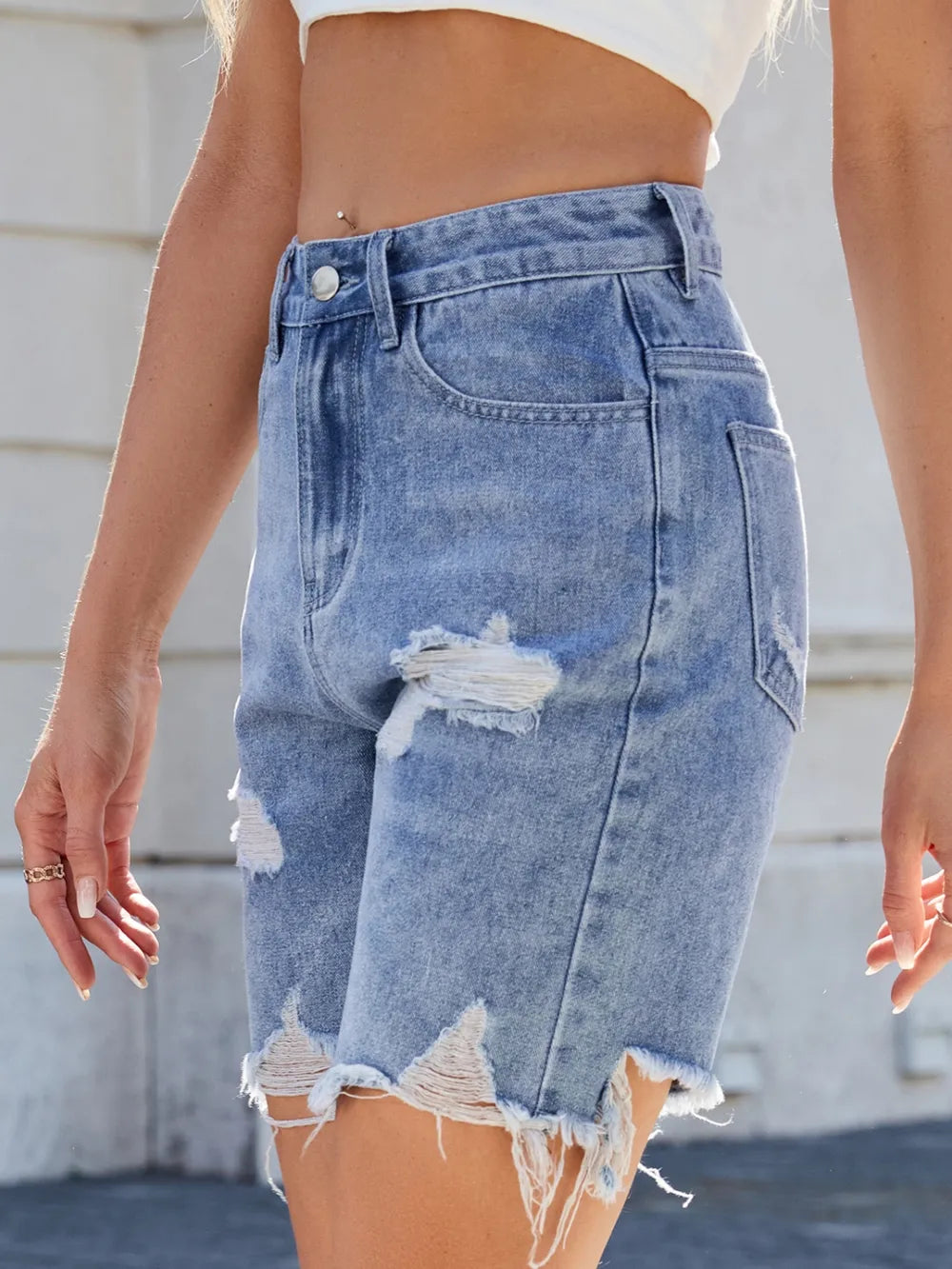 Close-up of a person wearing distressed denim shorts with a blurred background