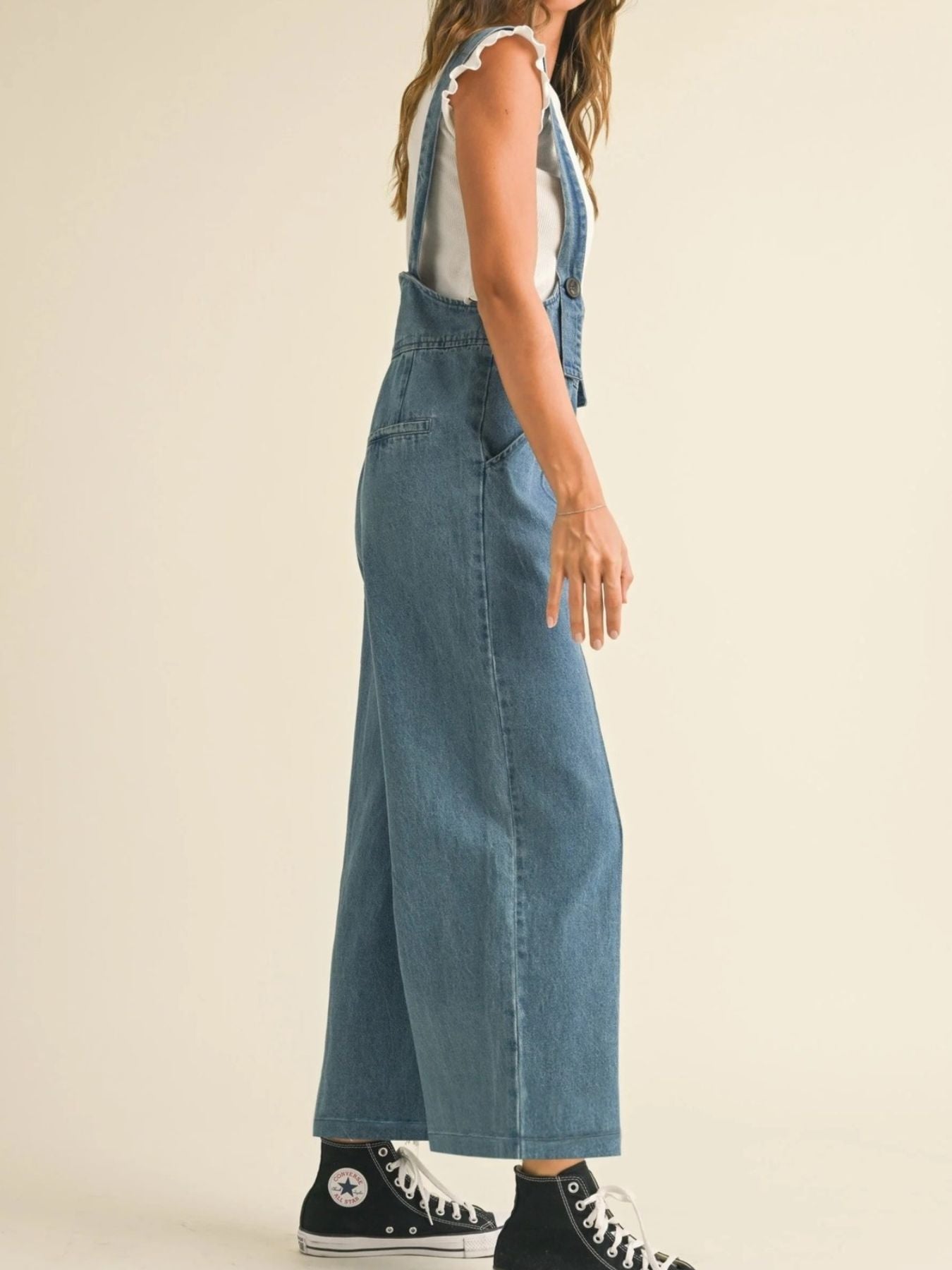 Person wearing blue denim overalls on a beige background