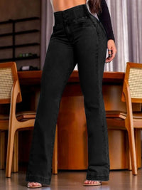 Person wearing black high-waisted pants standing in a room with wooden chairs and a table.