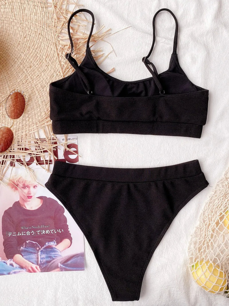 Black bikini set on a textured surface with a magazine and decorative items.