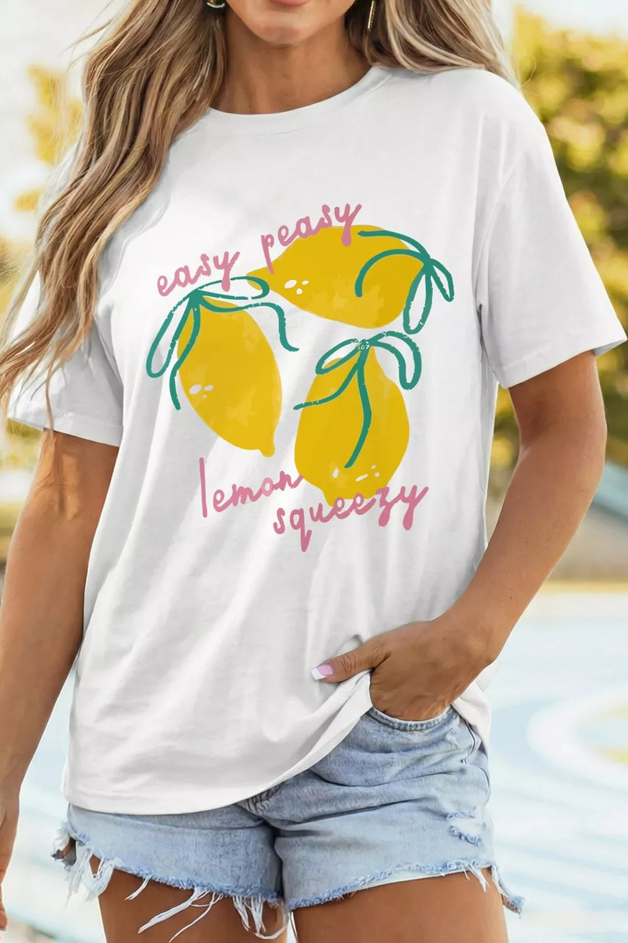 Person wearing a white t-shirt with lemon graphic and text, standing by a pool.