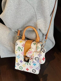 Designer handbag with colorful monogram pattern worn by a person in gray pants.