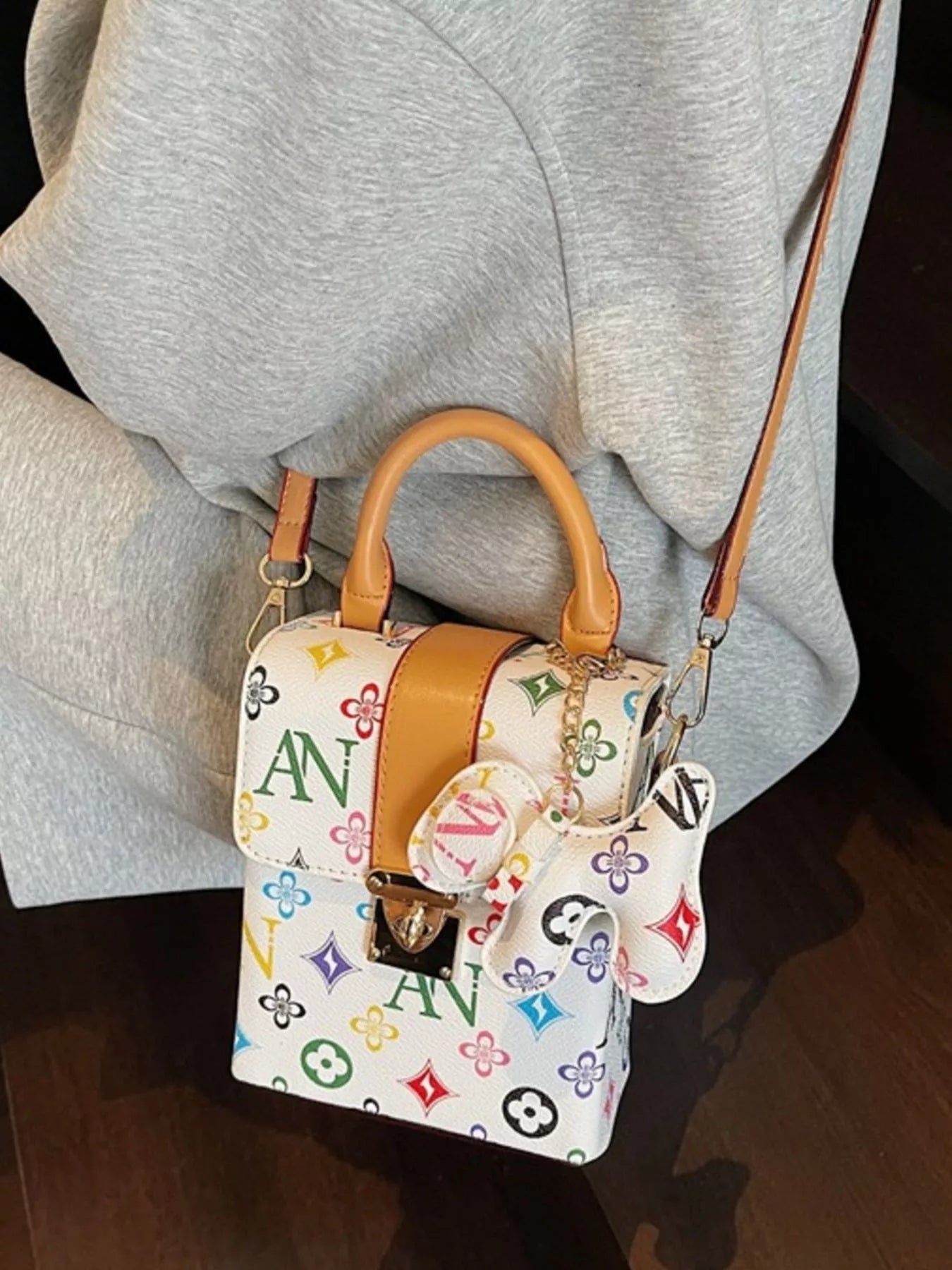 Designer handbag with colorful monogram pattern worn by a person in gray pants.