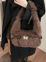 Brown fluffy handbag with decorative bow held by a person wearing a black coat.