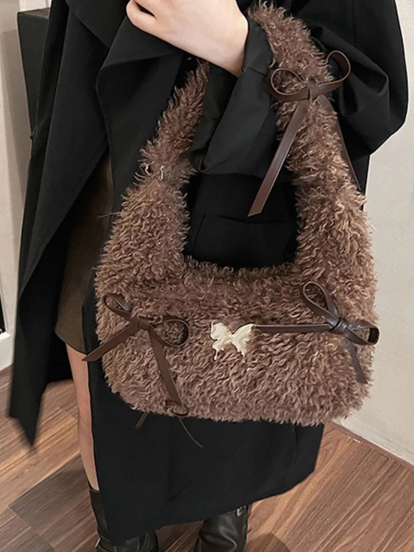 Brown fluffy handbag with decorative bow held by a person wearing a black coat.