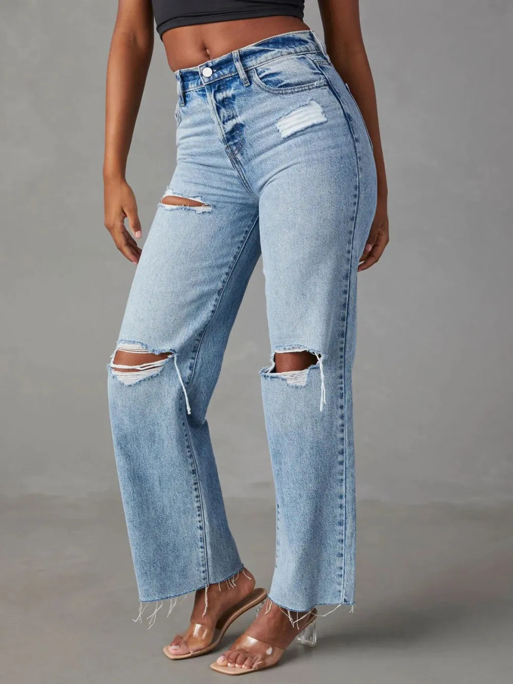 Light blue distressed jeans worn by a person on a gray background