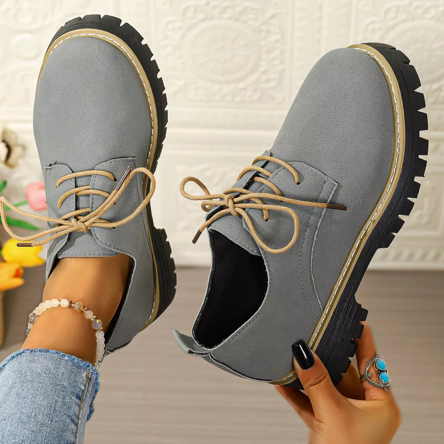 Gray lace-up shoes held by a person against a neutral background