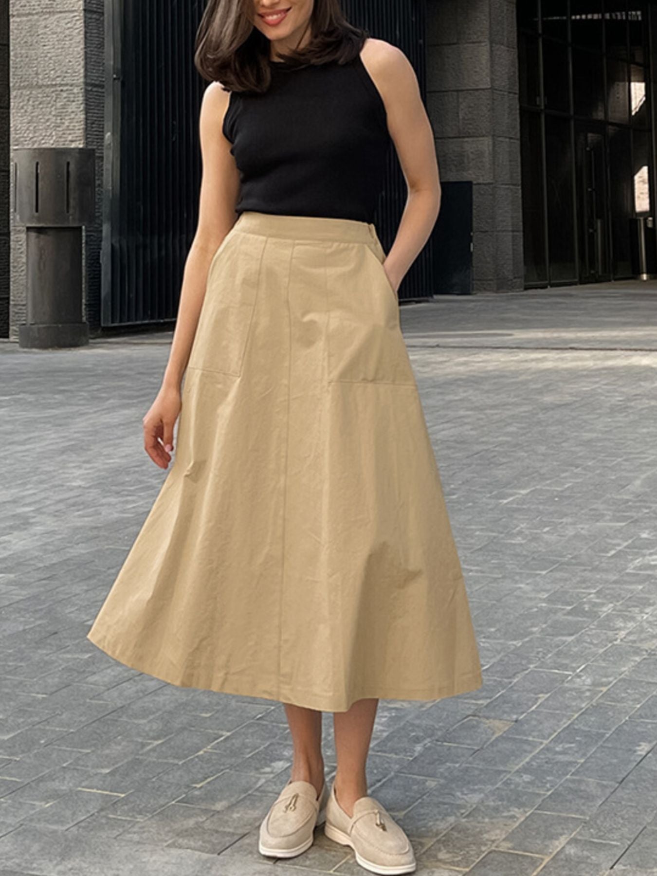 Woman wearing a black sleeveless top and beige skirt on a stone pavement.