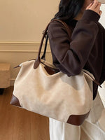 Person holding a beige handbag with brown accents indoors.