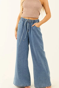 Person wearing blue denim wide-leg pants and a beige top on a white background