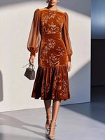 Woman wearing a brown velvet dress with floral embroidery against a neutral background