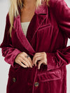 Close-up of a person wearing a burgundy velvet coat with a plain background