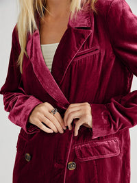 Close-up of a person wearing a burgundy velvet coat with a plain background
