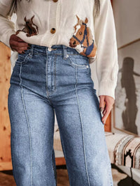 Person wearing a white cardigan with horse designs and blue jeans indoors.